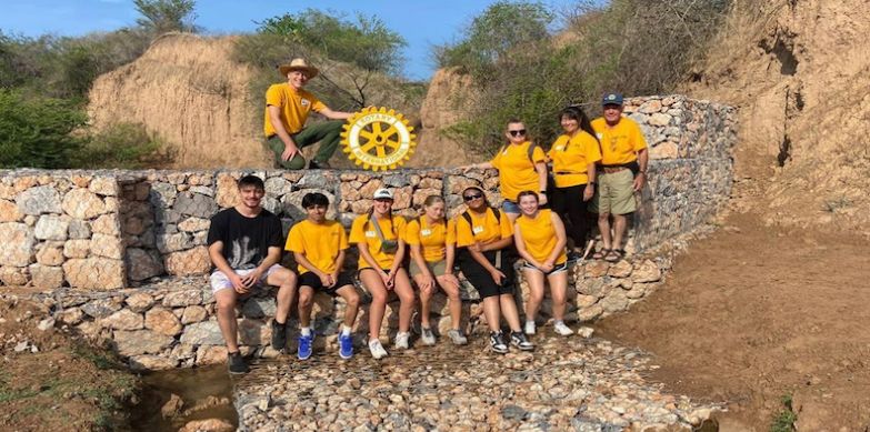 Group of people in yellow shirts sitting on stone wall.