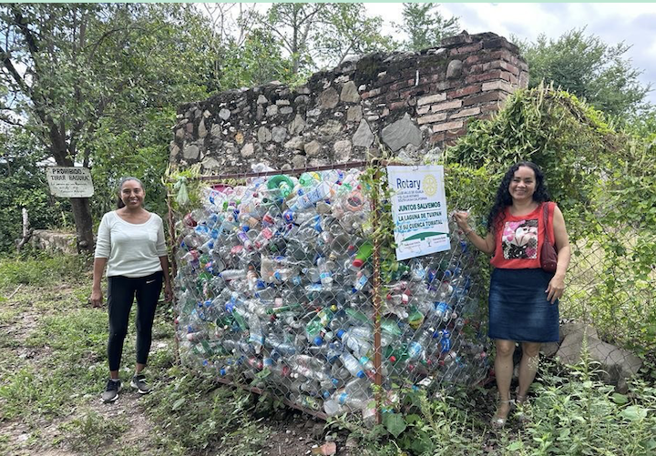 Two women standing next to hundreds of plastic bottles collected through the Global Grant project.