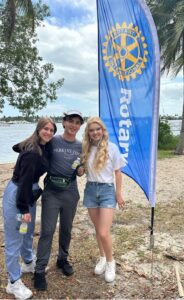 Three high school students standing in front of Rotary Flag and ocean